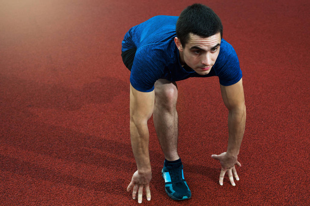 Молодой спортсмен низко начинает бегать по красной трекинговой синей рубашке
 - Фото, изображение