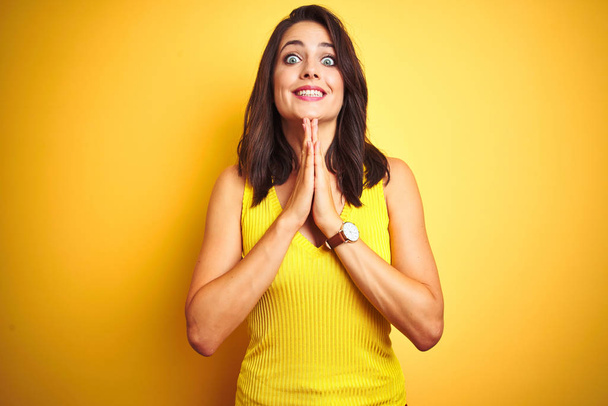 Young beautiful woman wearing t-shirt standing over yellow isolated background praying with hands together asking for forgiveness smiling confident. - Foto, immagini