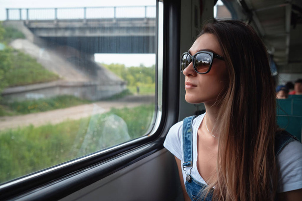 A young girl in sunglasses on the train looking out the window. Good mood in the journey - Foto, Imagem