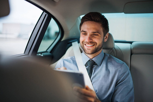 Businessman with tablet sitting on back seats in car, working. - Fotografie, Obrázek