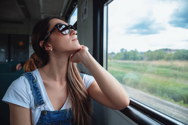 A young girl in sunglasses on the train looking out the window. Good mood in the journey - Fotoğraf, Görsel