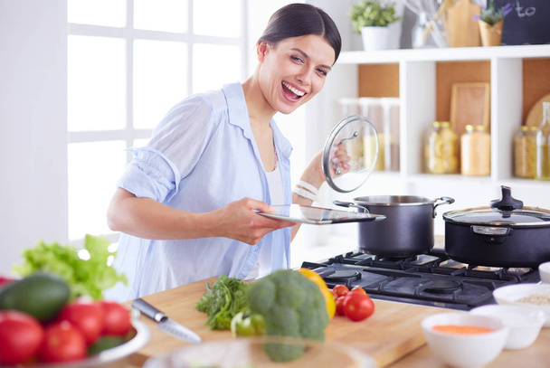 Молодая женщина, стоящая у плиты на кухне - Фото, изображение