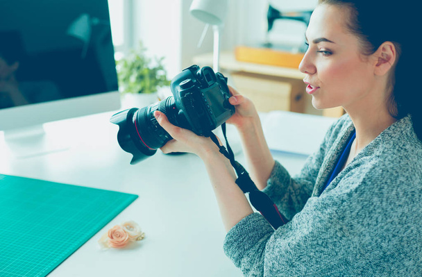 Nuori nainen suunnittelija seisoo työpaikan lähellä ja valokuvaus sen digitaalikamera
 - Valokuva, kuva