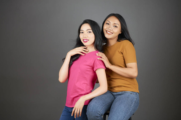 Портрет двох азіатських сестер посміхаючись і постановки на камеру разом над сірим фоном - Фото, зображення