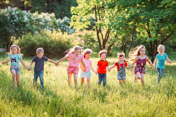 Large group of kids, friends boys and girls running in the park on sunny summer day in casual clothes . - Photo, Image