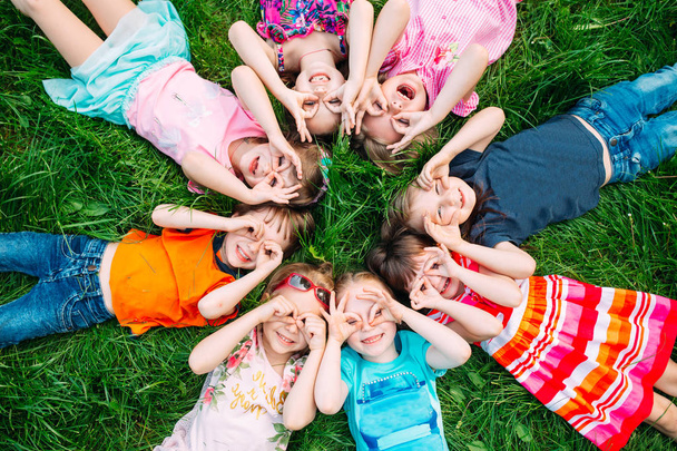 Eine Gruppe Kinder liegt auf dem grünen Rasen im Park. Die Interaktion der Kinder. - Foto, Bild