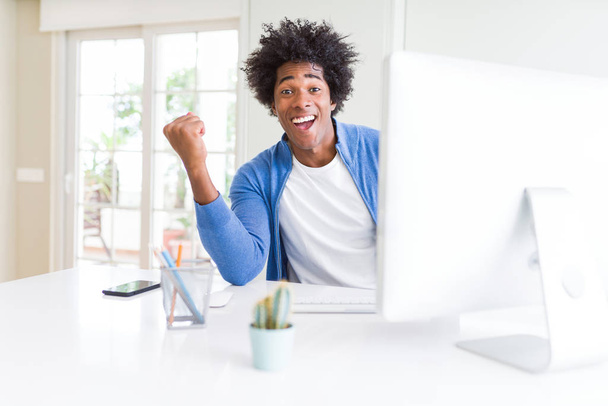 Hombre afroamericano trabajando usando computadora gritando orgulloso y celebrando la victoria y el éxito muy emocionado, animando emoción
 - Foto, imagen