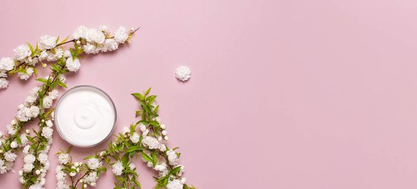 ビューティースパのコンセプト。ピンクの背景にクリームと春の白い花と開いたプラスチック容器フラットレイトップビュー。ハーブ皮膚科化粧品衛生クリーム、オーガニック化粧品ナチュラル - 写真・画像