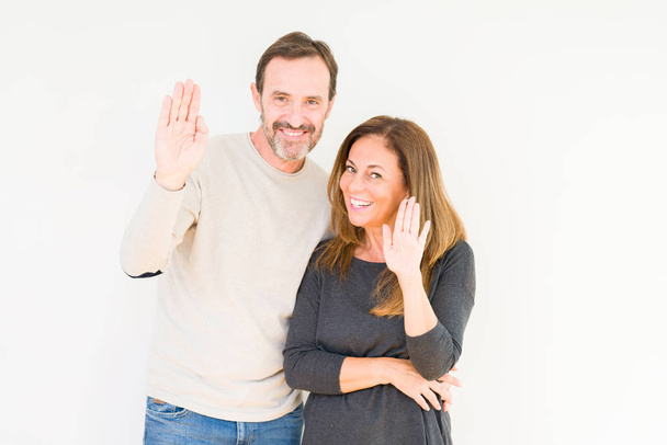Beautiful middle age couple in love over isolated background Waiving saying hello happy and smiling, friendly welcome gesture - Foto, afbeelding