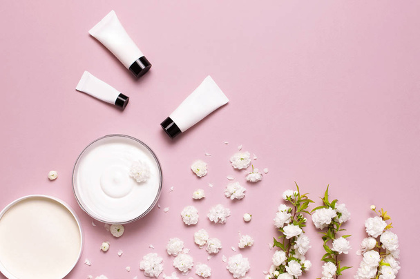 ビューティースパのコンセプト。クリーム、化粧品ボトル容器、ピンクの背景に春白い花と開いたプラスチック容器フラットレイトップビュー。ハーブ皮膚科化粧品衛生クリームオーガニック - 写真・画像