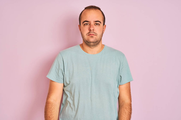 Νέος άντρας φορώντας μπλε casual t-shirt στέκεται πάνω από απομονωμένο ροζ φόντο χαλαρή με σοβαρή έκφραση στο πρόσωπο. Απλό και φυσικό κοιτάζοντας την κάμερα. - Φωτογραφία, εικόνα
