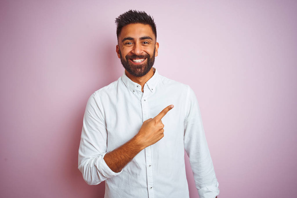 Young indian businessman wearing elegant shirt standing over isolated pink background cheerful with a smile of face pointing with hand and finger up to the side with happy and natural expression on face - Photo, Image