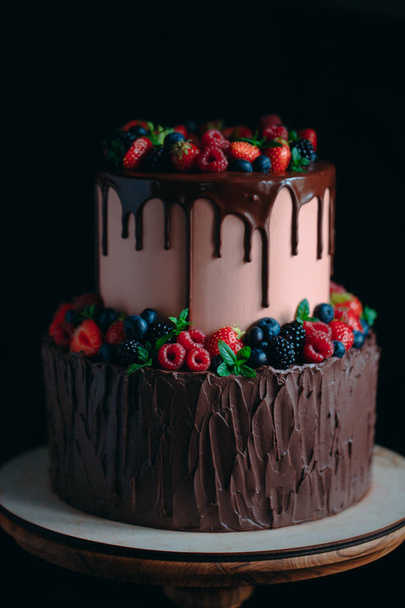 Fruit chocolate cake on wooden stand on black background. - Zdjęcie, obraz