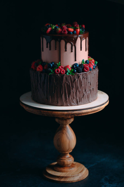 Fruit chocolate cake on wooden stand on black background. - Фото, изображение
