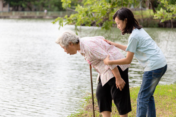 Asian senior grandmother about to throw up,vomit,puke retch barf,feeling sick from indigestion or food poisoning,elderly woman with child girl or granddaughter helping,care her in outdoor park,health care concept  - Photo, Image