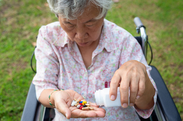 Pillole o capsule di medicina per donne anziane asiatiche in mano, assunzione di pazienti malati, assunzione di vitamine, antibiotici, antidolorifici, integratori alimentari anziani in un parco all'aperto per sedie a rotelle, assistenza sanitaria, concetto di medicina
 - Foto, immagini