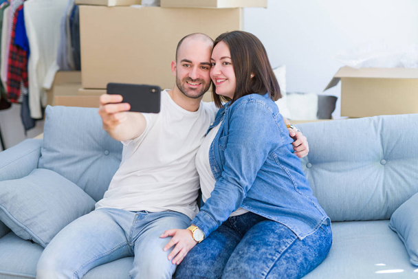 Молодая пара, сидящая на диване в новом доме, делает селфи фо
 - Фото, изображение