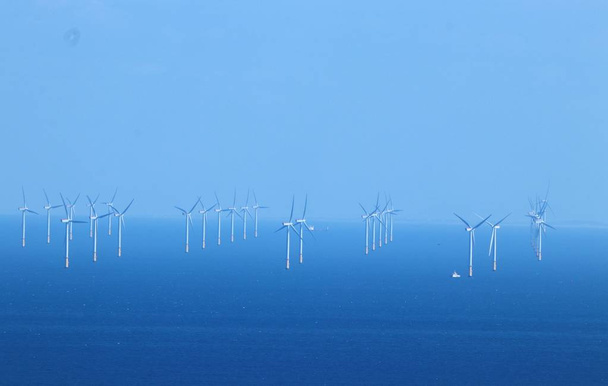 Белые ветряные турбины в голубом море с голубым небом в Гвинт и мистер Северный Уэльс. Ярко-синее море и небо контрастирует с белыми ветряными турбинами и маленькой белой лодкой технического обслуживания. Образ возобновляемой, устойчивой, альтернативной генерации электроэнергии
. - Фото, изображение
