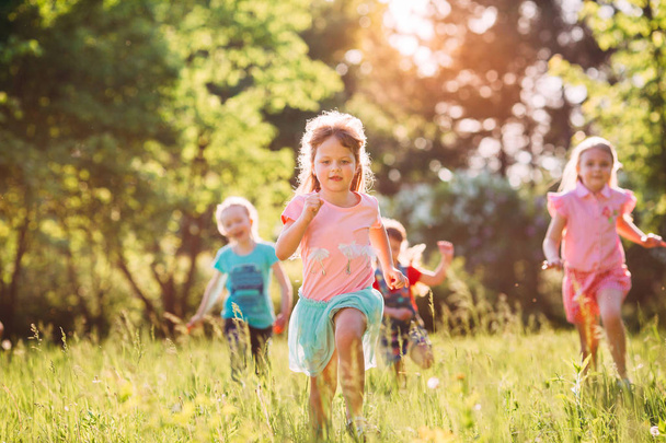 Nagy csoport gyerekek, barátok fiúk és lányok fut a parkban a napsütéses nyári napon alkalmi ruhák . - Fotó, kép