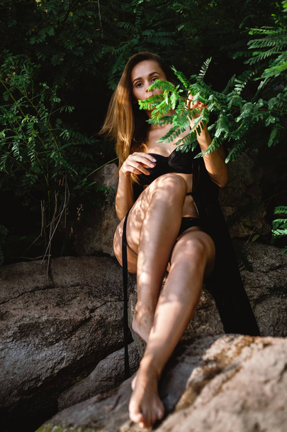Beautiful model in a black swimsuit and pareo posing on the coast. - Fotoğraf, Görsel