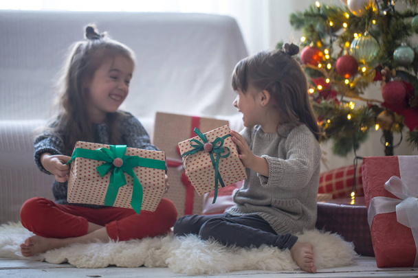 Pretty küçük kızlar bir hediye kutuları tutan ve ışık arka plan üzerinde evde gülümseyen - Fotoğraf, Görsel