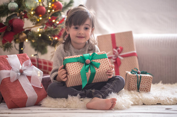 Jolie petite fille tient une boîte cadeau et sourit tout en étant assise sur son lit dans sa chambre à la maison
 - Photo, image