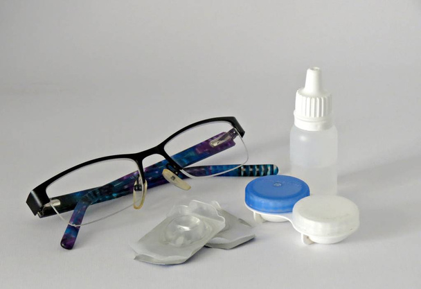 Gafas para ojos, lentes de contacto, estuche y botella con solución sobre fondo gris
. - Foto, Imagen
