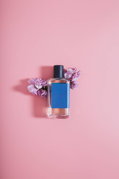 Бутылка парфюмерии на розовом фоне с цветами
 - Фото, изображение