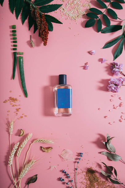Perfume bottle with blue sticker in flowers on pink background. Spring background with aroma parfume. Flat lay - Fotoğraf, Görsel