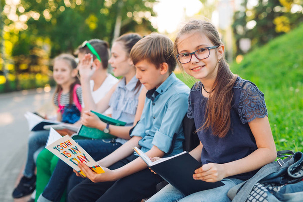 Happy Schoolmates Portrait. Schoolmates seating with books in a wooden bench in a city park and studying on sunny day. - Foto, imagen