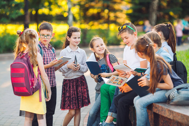 Happy Schoolmates muotokuva. Koulukaverit istuu kirjoja puinen penkki kaupungin puistossa ja opiskelee aurinkoisena päivänä. - Valokuva, kuva