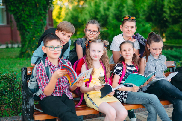 Happy Schoolmates Portrait. Schoolmates seating with books in a wooden bench in a city park and studying on sunny day. - Fotografie, Obrázek