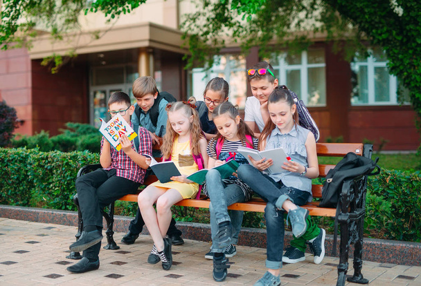 Happy Schoolmates Portrait. Schoolmates seating with books in a wooden bench in a city park and studying on sunny day. - Foto, imagen