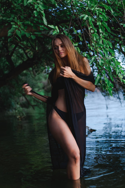 Beautiful model in a black swimsuit and pareo posing on the coast. - Valokuva, kuva