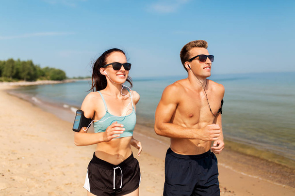 couple with phones and arm bands running on beach - Foto, immagini