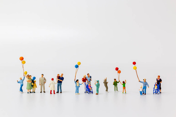 Miniatuur mensen houden ballon geïsoleerd op witte achtergrond  - Foto, afbeelding