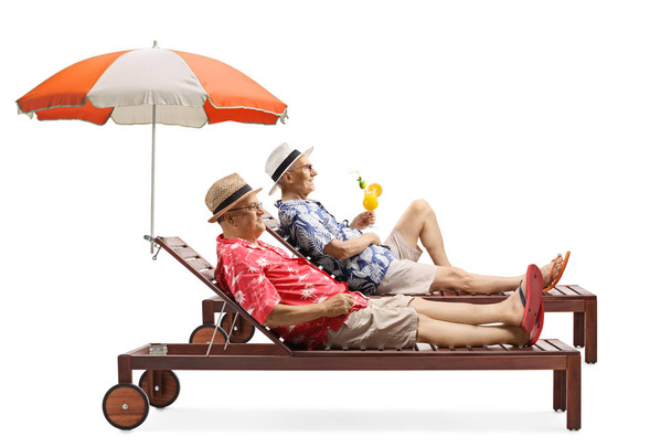 Two senior men on vacation enjoying a cocktail on a sunbed under - 写真・画像