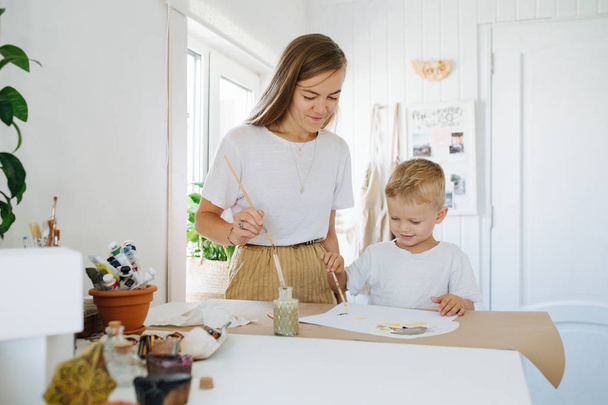 Young mother and first grade son are painting together at home - Photo, image