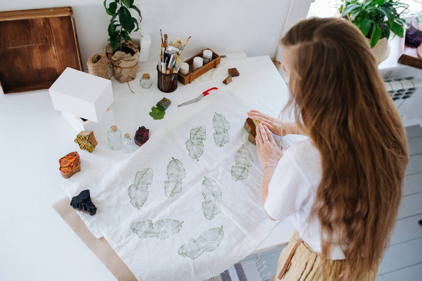 Young woman making green leaf-shaped prints on fabric with wooden stamp. - Foto, Imagem