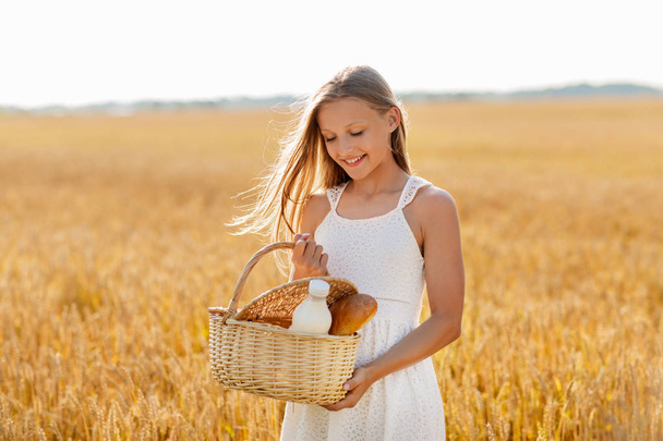 girl with bread and milk in basket on cereal field - Foto, imagen