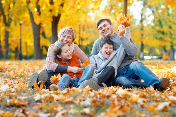 Gelukkige familie zittend op gevallen bladeren, spelen en plezier in de herfst City Park. Kinderen en ouders samen met een mooie dag. Fel zonlicht en gele bladeren op bomen, herfst seizoen. - Foto, afbeelding