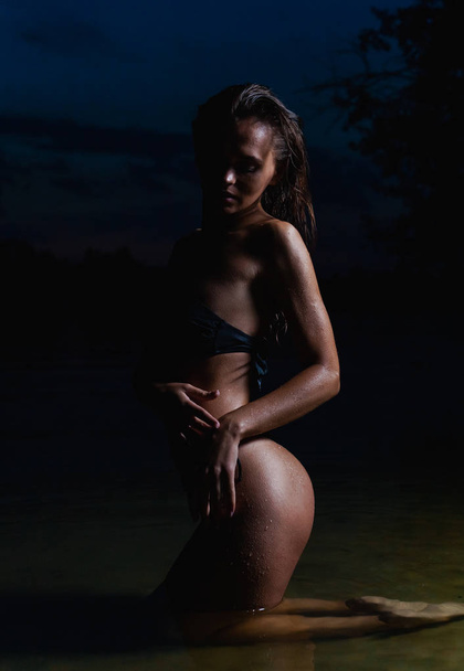 水の中で美しいモデル。夜のための黒いビキニ水着で、水泳とポーズ. - 写真・画像