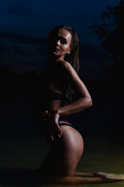 Beautiful model in the water. In a black bikini swimsuit for the night, swimming and posing. - Foto, immagini