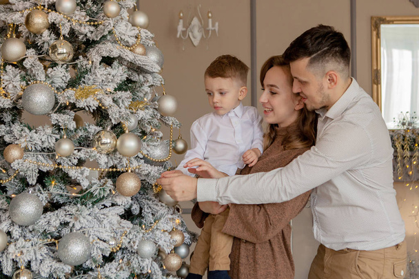 Parents and their little son decorating Christmas tree with toys and garlands - Φωτογραφία, εικόνα