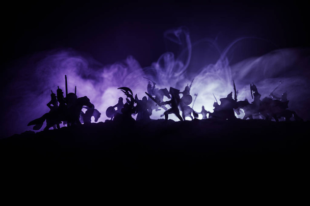 騎兵と歩兵と中世の戦闘シーン。別々のオブジェクトとしてのフィギュアのシルエットは、中世の城と暗い色調の霧の背景に戦士の間で戦います. - 写真・画像
