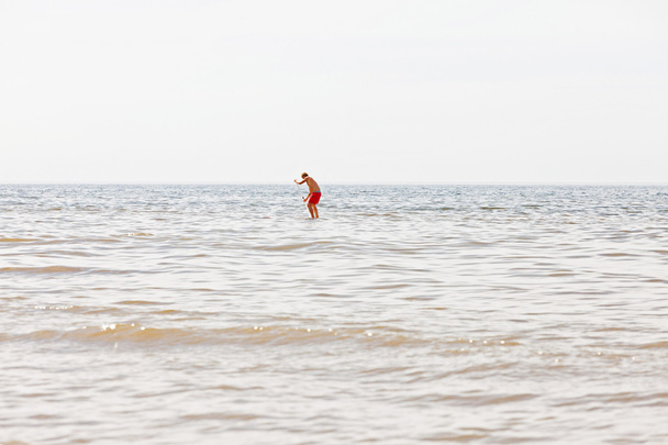 Un hombre en la tabla de remo remando hacia el océano. ¿Qué pasa? Nublado s
 - Foto, imagen