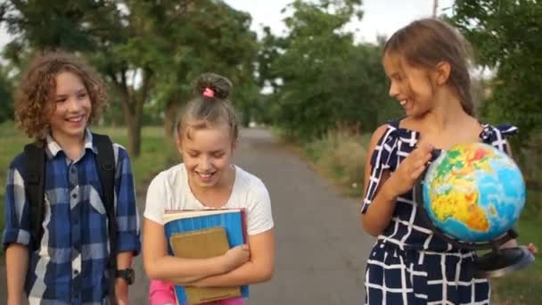 Lovely curly boy and his two girlfriends go to school. The child talks enthusiastically, the girls are listening. A classmate holding a globe in her hands - Footage, Video