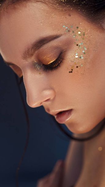 Charming girl with trendy glitter makeup, fashionable make-up with gold glitter on the cheekbones and near the eyes. - 写真・画像