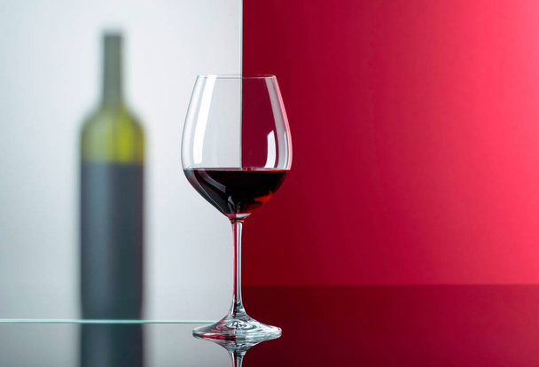 Μπουκάλι και γυαλί κόκκινου κρασιού σε μαύρο αντανακλαστικό φόντο.  - Φωτογραφία, εικόνα