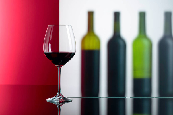 Flessen en glas rode wijn op een zwarte reflecterende achtergrond.  - Foto, afbeelding